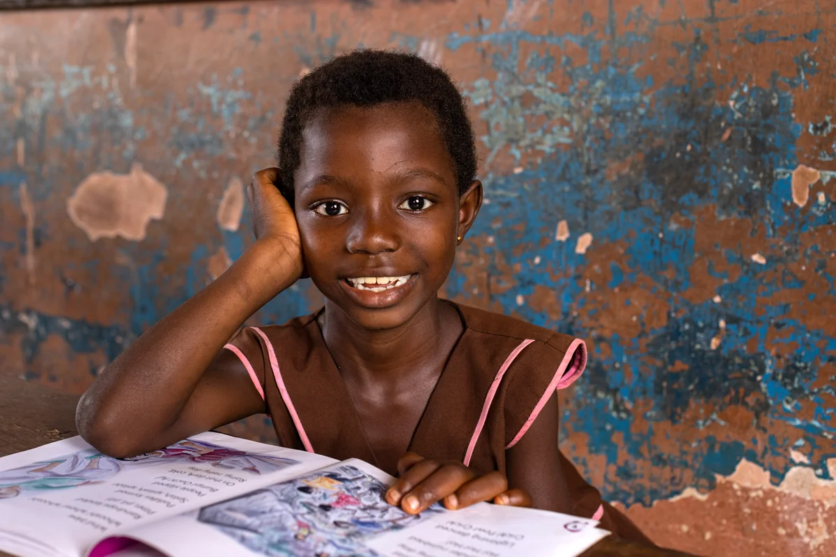 Smiling student with an open book in a Teaching and Learning in Fragile Contexts classroom