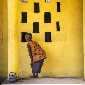 Child In Front Of Bright Yellow Wall Looking Through Square Windows
